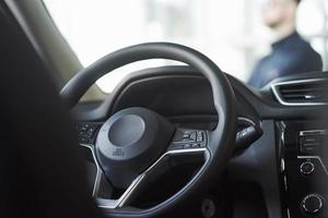 dentro de un auto negro nuevo. interiores de lujo. el hombre se para frente al automóvil foto