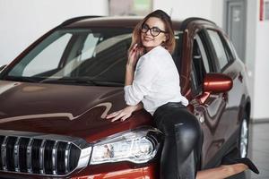 postura sexual mujer bonita con falda negra cerca de un auto nuevo en el salón del automóvil foto