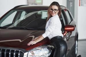 Hot woman. Pretty girl in black skirt posing near brand new car in automobile salon photo