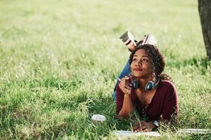 Writer thinks how to finish the chapter. Cheerful african american woman in the park at summertime photo