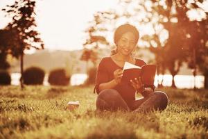 Nice nature and lake behind. Cheerful african american woman in the park at summertime photo