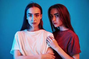 Different clothes. Studio shot indoors with neon light. Photo of two beautiful twins