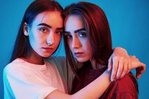 They love each other. Studio shot indoors with neon light. Photo of two beautiful twins