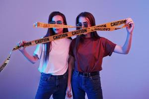 Keep back. Studio shot indoors with neon light. Photo of two beautiful twins