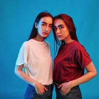 In front of each other. Studio shot indoors with neon light. Photo of two beautiful twins