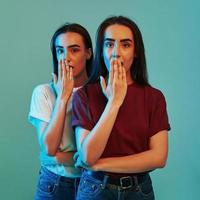 Shocked sisters. Studio shot indoors with neon light. Photo of two beautiful twins