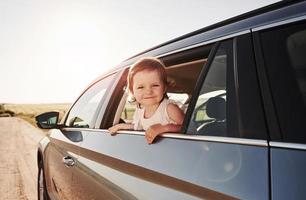 niño positivo. un niño lindo mira a través de la ventana de un auto nuevo y moderno en un día soleado foto