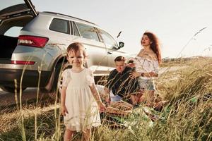 Enjoying nature. Family have picnic at countryside near silver automobile at sunset photo