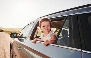 Cute kid looks through the window of brand new modern car at sunny day photo