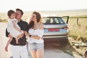 aman a su hijo. la familia pasa un buen rato en el campo cerca del automóvil plateado al atardecer foto