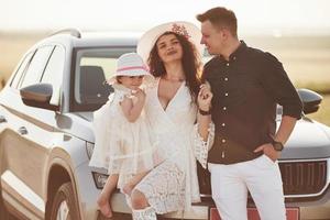 Family photo. People have some good time at countryside near silver automobile at sunset photo