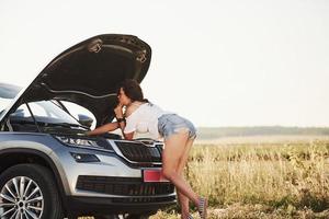 Made it by yourself. Hot woman open hood of her broken car and fixes it at countryside photo