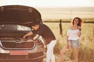 sólo dame un par de minutos. el hombre repara el coche de la chica con el pelo rizado. asistencia mecanica foto