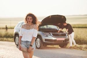 Spontaneous breakdown. Man repairs car of girl with curly hair. Mechanical assistance photo