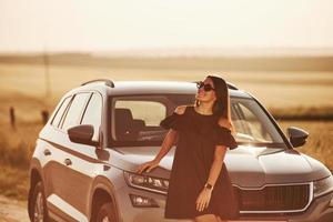 In eyewear. Girl in black clothes posing near the modern luxury automobile outdoors photo