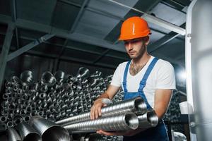 Takes ventilation pipes. Man in uniform works on the production. Industrial modern technology photo