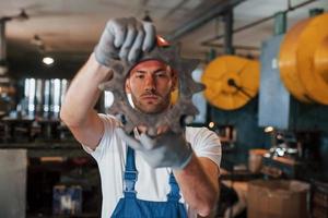 mira a través de nuevos detalles. hombre en uniforme trabaja en la producción. tecnología industrial moderna foto