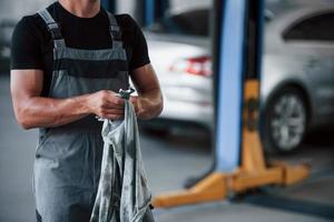 Preparing for the job. Man in black shirt and grey uniform stands in garage after repairing broken car photo