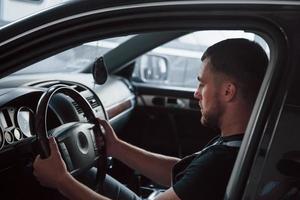 Guy test brand new car in the garage. Black colored interior. Hands on steering wheel photo