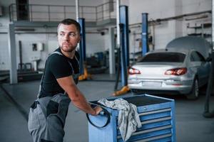 Moves to the car. Male mechanic use different tools to repair broken automobile in garage photo