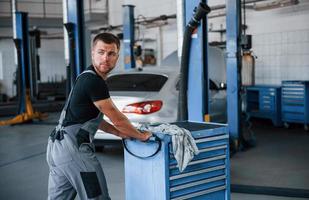 One person only. Male mechanic use different tools to repair broken automobile in garage photo