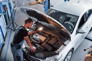 Man in grey uniform repairs white automobile indoors photo