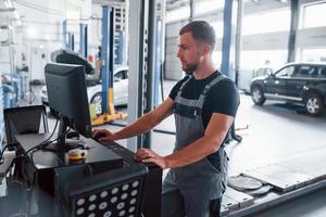Searching information. Man at the workshop in uniform use computer for his job for fixing broken car photo