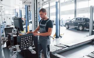 Looks at keyboard. Man at the workshop in uniform use computer for his job for fixing broken car photo