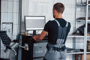 información en el monitor. hombre en el taller con computadora de uso uniforme para su trabajo para arreglar un auto roto foto