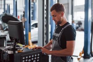 Diagnostic pc. Man at the workshop in uniform use computer for his job for fixing broken car photo