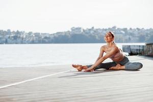 At free time. Young woman with slim type of body does exercises against lake photo