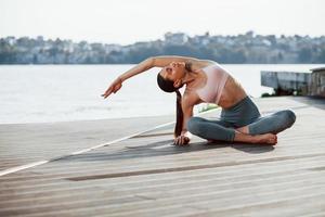 One person only. Young woman with slim type of body does exercises against lake photo