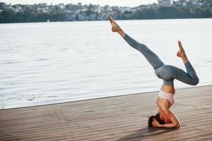 experiencia necesaria para hacer esto. mujer joven con cuerpo delgado hace ejercicios contra el lago foto