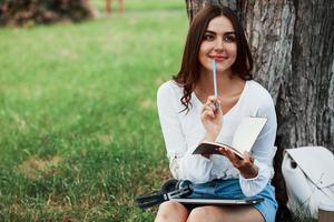 Writter thinks how to finish the chapter. Young woman have weekend and sits in the park at daytime photo