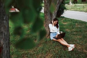 Having good mood. Young woman have weekend and sits in the park at daytime photo