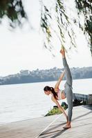 Professional trainer. Young woman with slim type of body does exercises against lake photo
