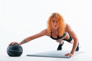 With black soccer ball. Redhead female bodybuilder is in the studio on white background photo