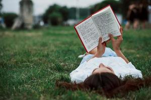 Adult person reads notepad. Girl lying down on the green grass and have a rest photo