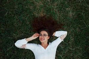 Wearing glasses. Girl lying down on the green grass and have a rest photo