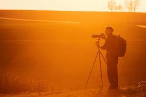 Photographer with professional equipments makes photos. Stands in the field illuminated by sunlight photo