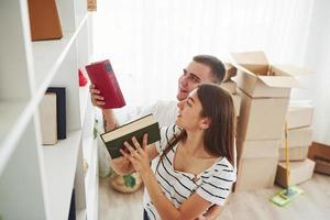 cada libro debe estar en su lugar correcto. pareja joven alegre en su nuevo apartamento. concepción de movimiento foto