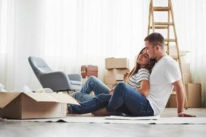 Empty room with boxes and ladder. Cheerful young couple in their new apartment. Conception of moving photo