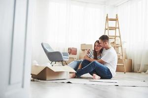 Empty room with boxes and ladder. Cheerful young couple in their new apartment. Conception of moving photo