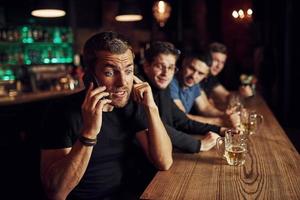 el hombre habla por teléfono. tres aficionados al deporte en un bar viendo fútbol. con cerveza en las manos foto