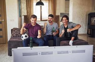 emocionados tres amigos viendo fútbol en la televisión en casa juntos foto