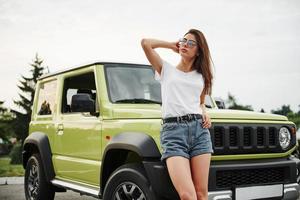 se encuentra cerca de un vehículo nuevo. Pretty Woman en el coche moderno verde posando para la cámara foto