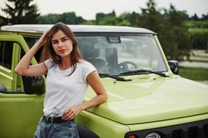 Stands near new vehicle. Pretty woman in the green modern car posing for the camera photo