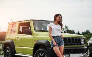 se encuentra cerca de un vehículo nuevo. Pretty Woman en el coche moderno verde posando para la cámara foto