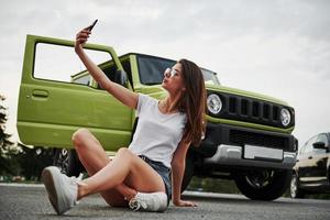 Making selfie. Sits and resting near new vehicle. Pretty woman in the green modern car posing for the camera photo