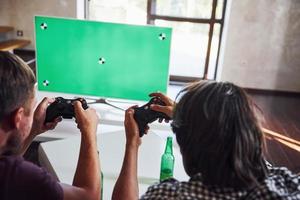 cerveza en la mesa. grupo de amigos se divierten jugando juegos de consola en el interior de la sala de estar foto